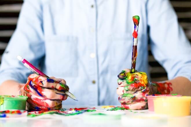 A man holding paintbrushes with paint on his hands